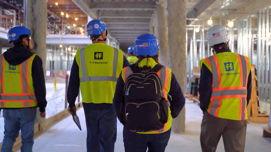 A team of four workers in F+F Mechanical safety gear walks through an indoor construction site.