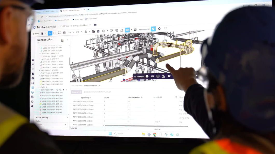 Two workers point at a complex 3D BIM piping model on a monitor using Trimble Connect2Fab software.