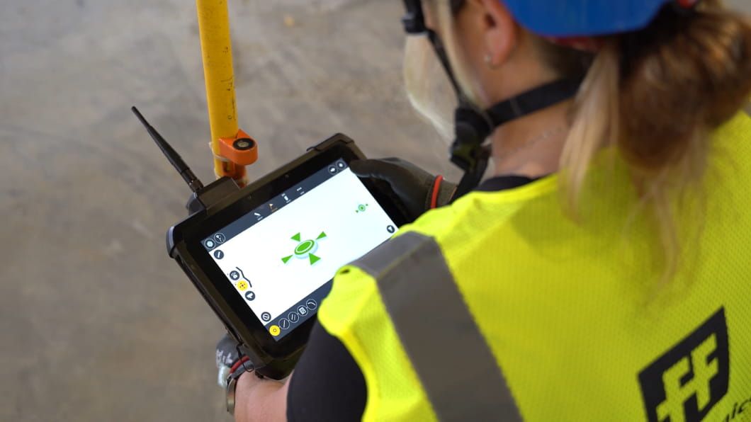 A F+F Mechanical worker in a safety vest uses a rugged tablet to manage digital layout and targeting on a construction site.